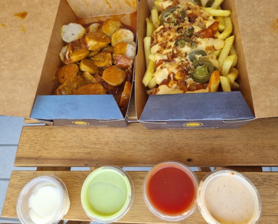 Double Currywurst und Loaded Fries Chili Cheese von Pommesfreunde Stuttgart Mitte, dazu Ketchup, Majo, Wasabi Majo und Samourai Soße in Plastikbechern